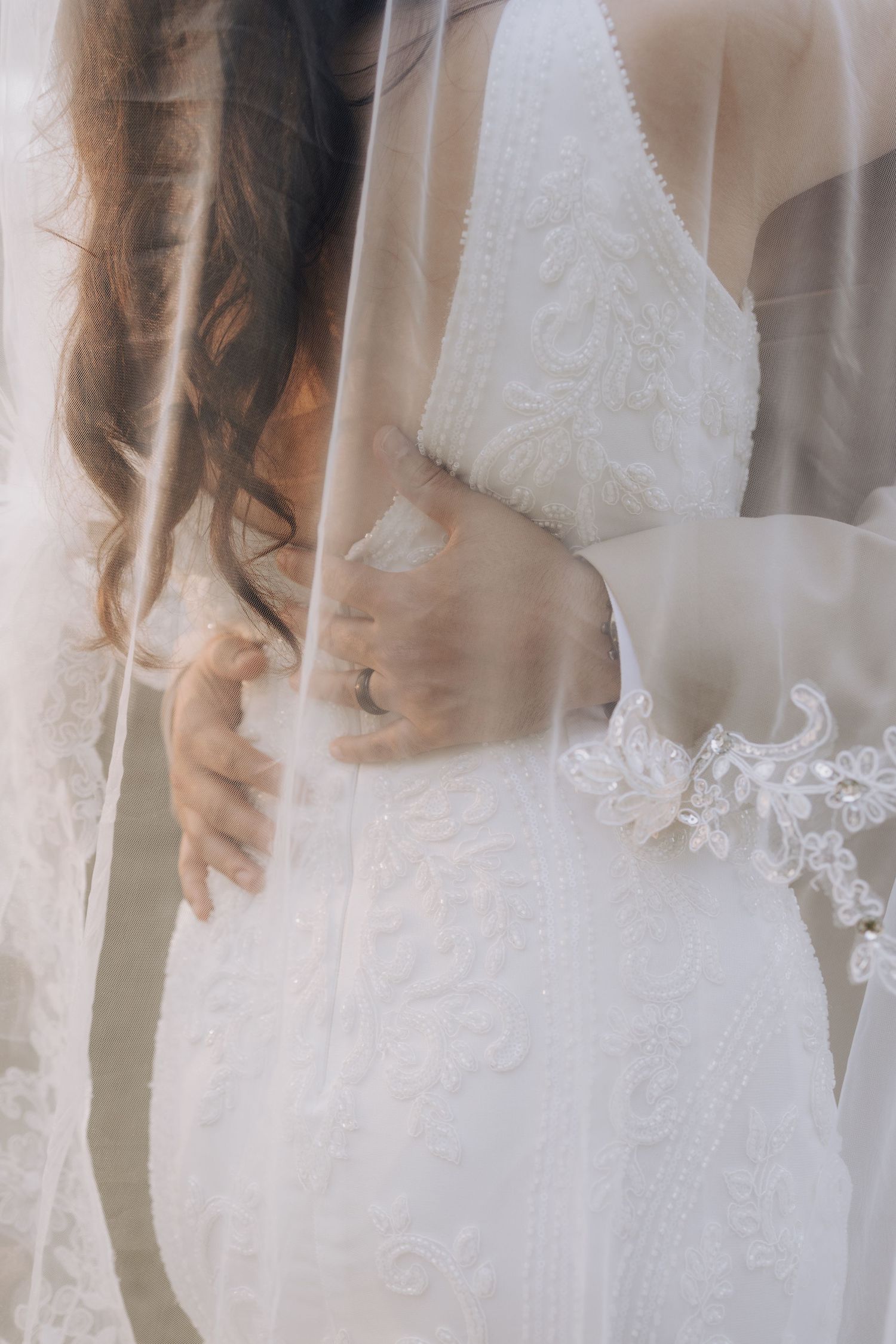 Close-up detail of a white lace wedding dress with delicate embellishments.