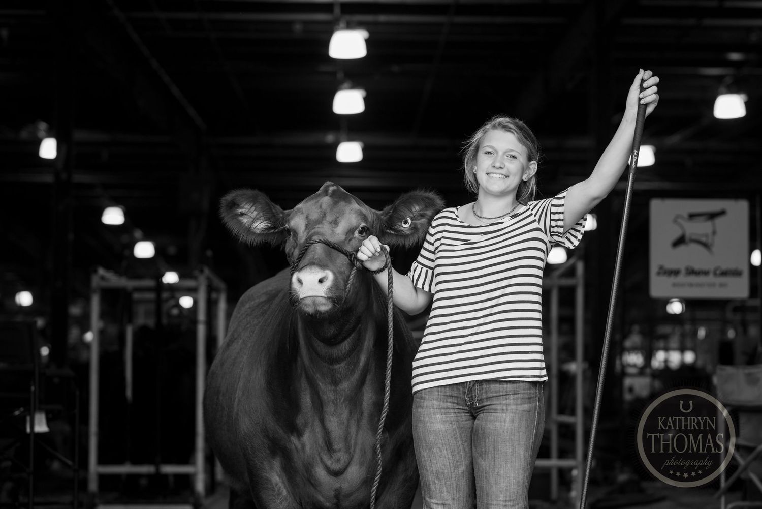 A black and white photo shows a person posing with their show cow in a barn.