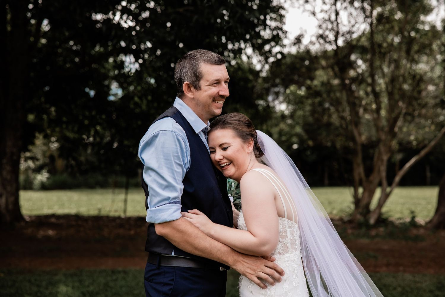 Couple shares intimate moment and laughter during outdoor wedding portraits.