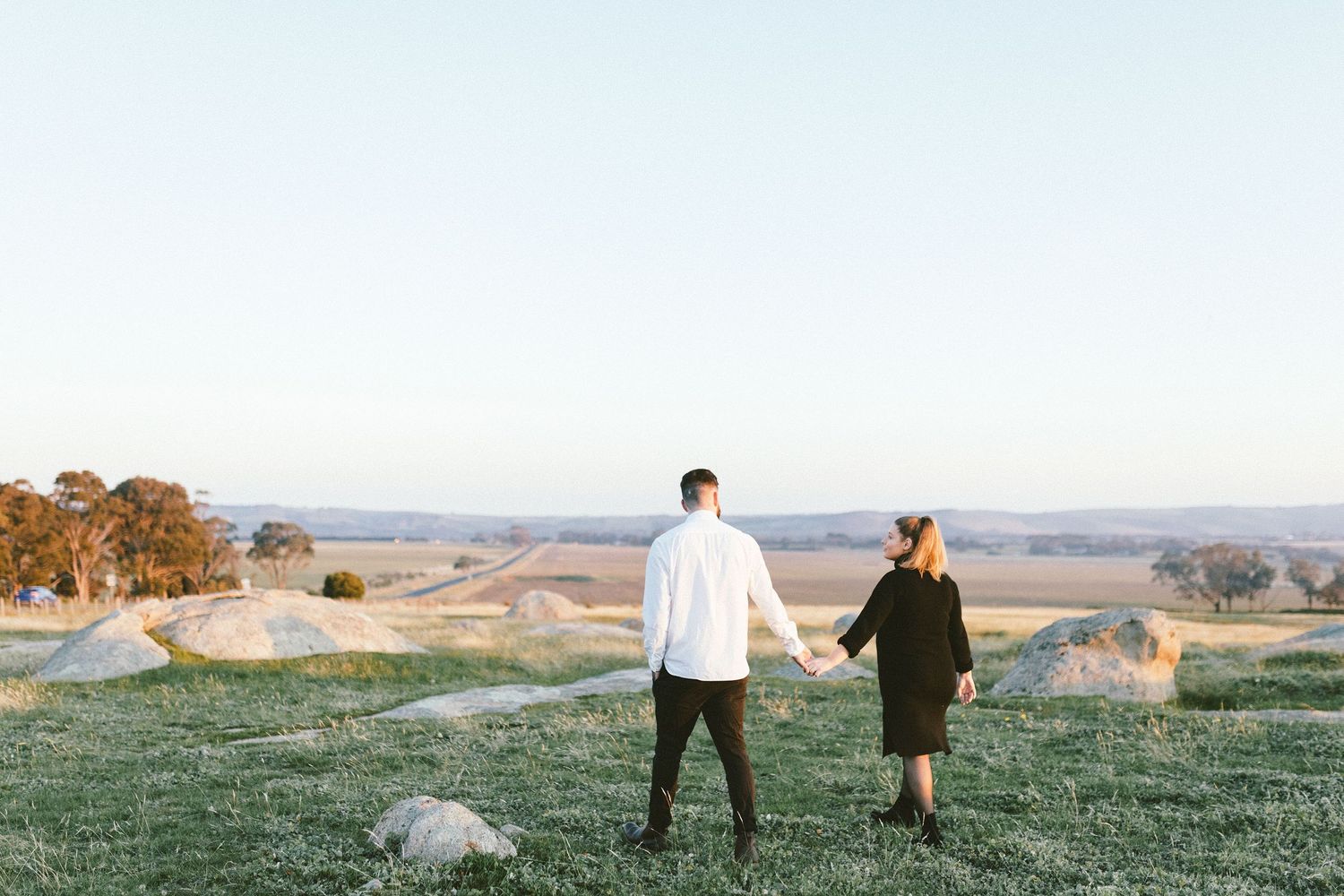 A couple enjoys a peaceful moment on a grassy hill overlooking a rural landscape.