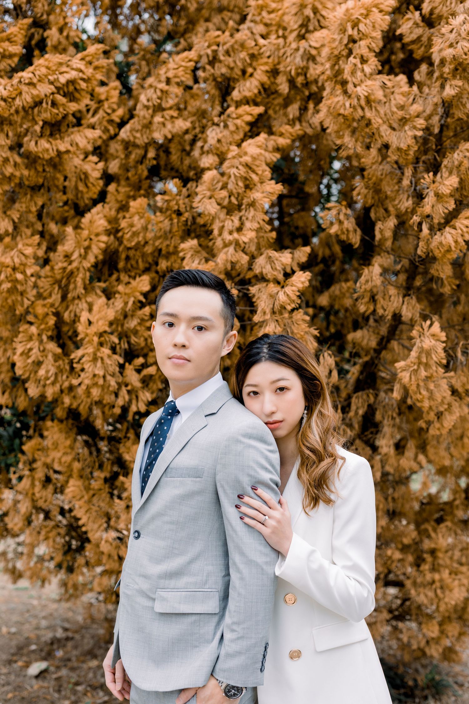 A couple embraces against a backdrop of golden autumn foliage while wearing formal attire.
