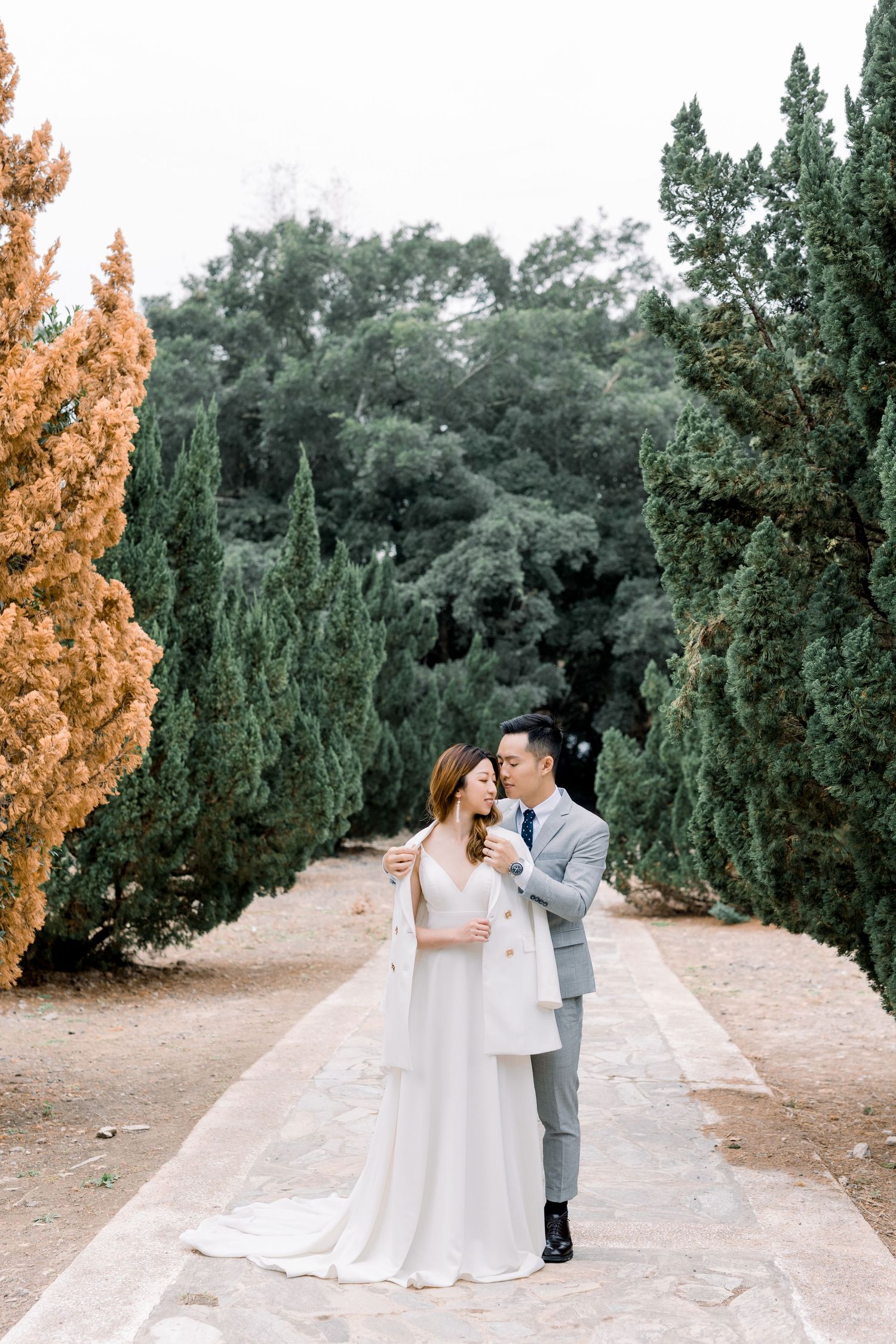 A romantic outdoor wedding photoshoot with lush greenery and cypress trees in the background.
