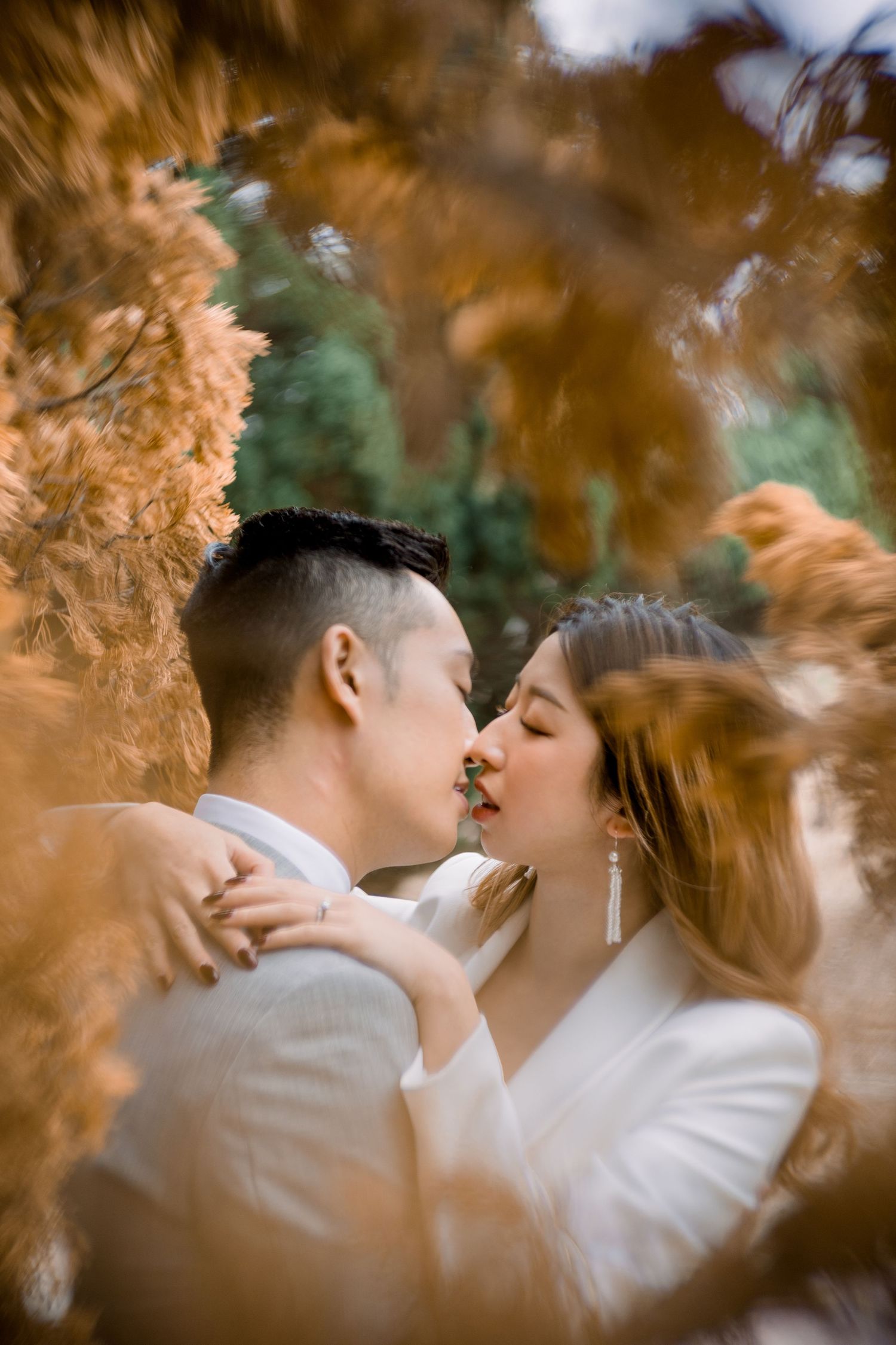 An intimate kiss captured through golden autumn branches.