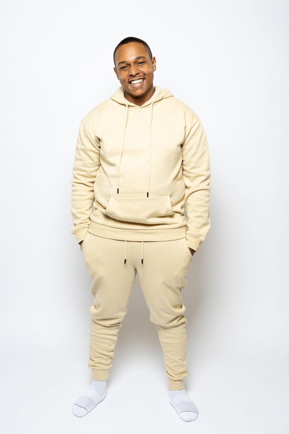 Man poses in comfortable beige sweatsuit and white socks against white background.