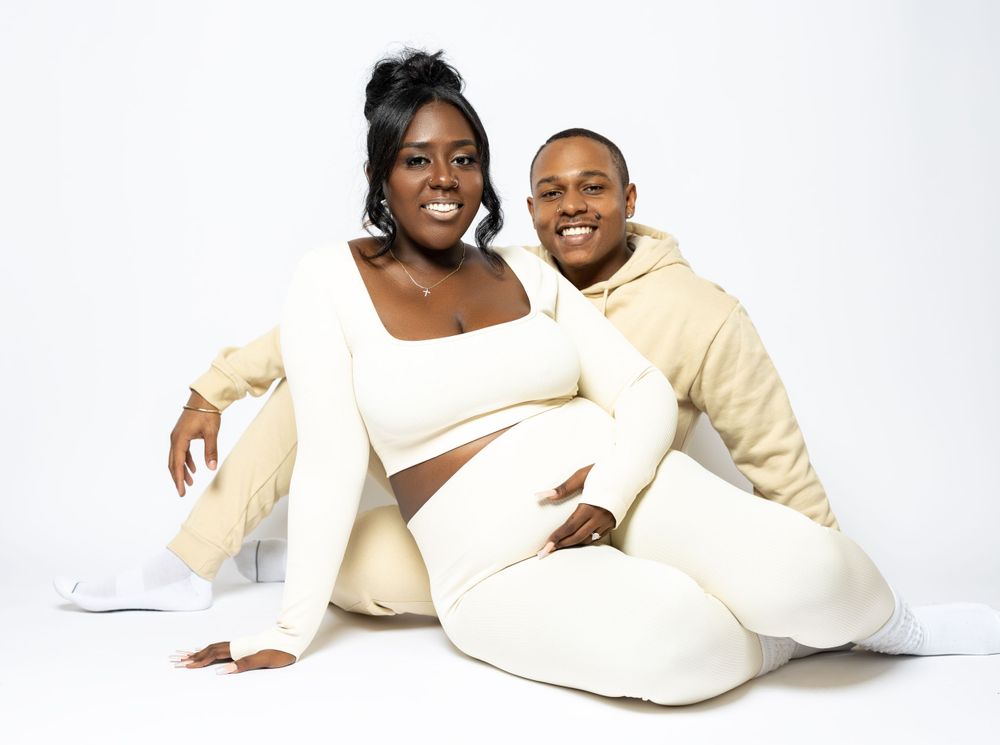 Joyful maternity portrait with couple in cream colored loungewear against white background.