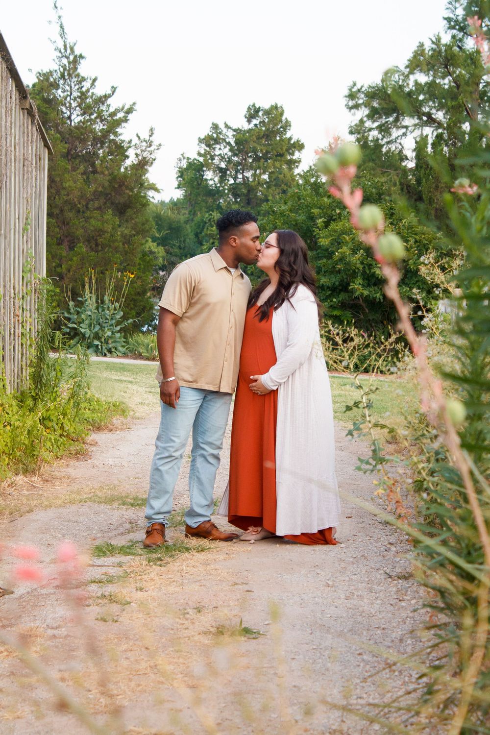 A romantic couple sharing a tender moment on a garden path surrounded by greenery.