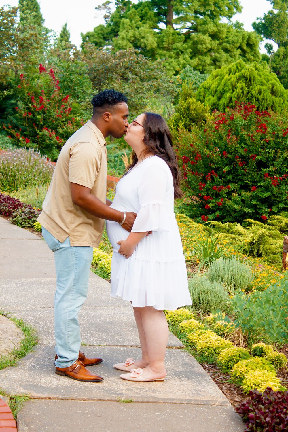 A loving couple embraces on a garden pathway surrounded by colorful flowers and landscaping.