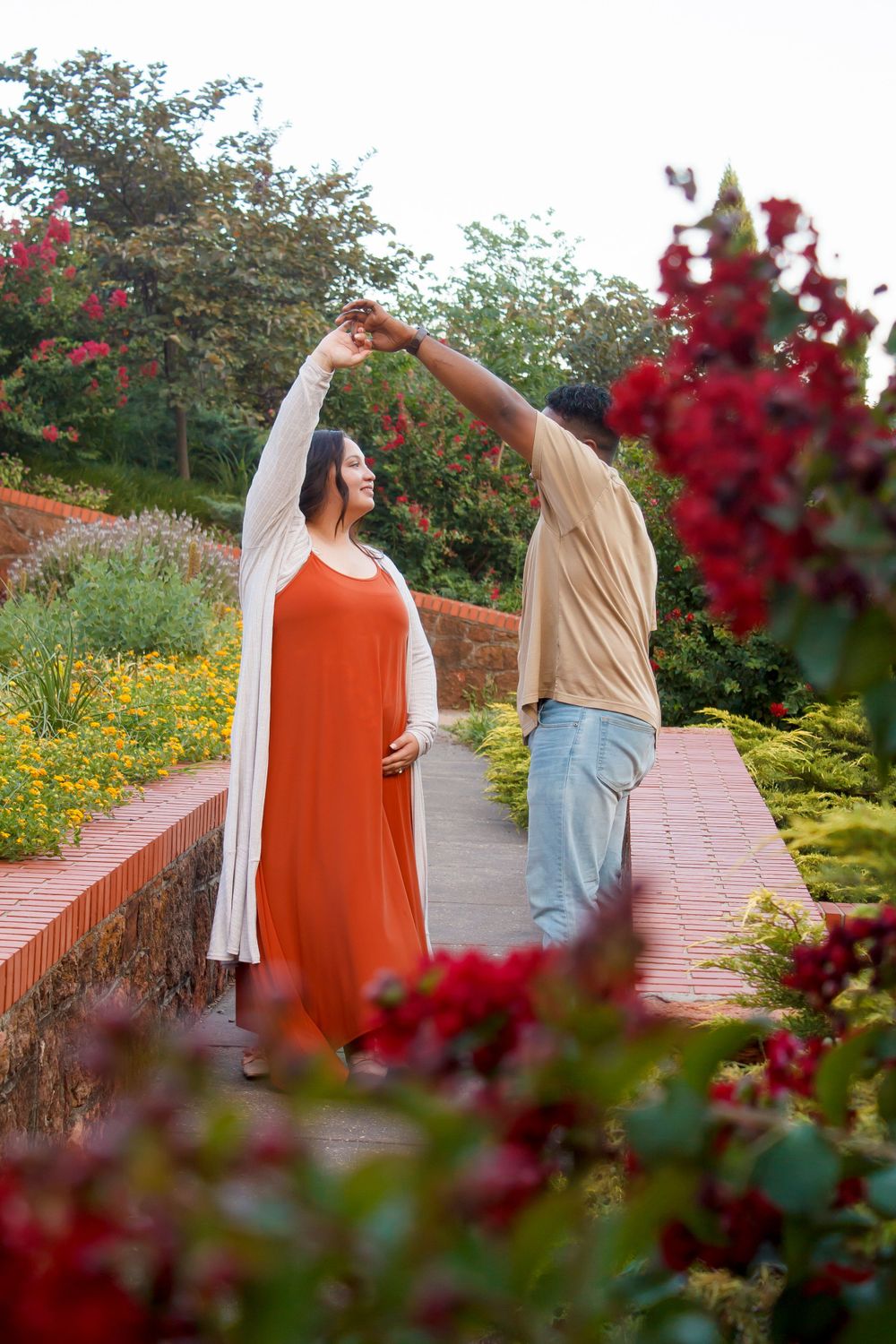 A couple dancing together on a brick pathway surrounded by vibrant red flowers and greenery.