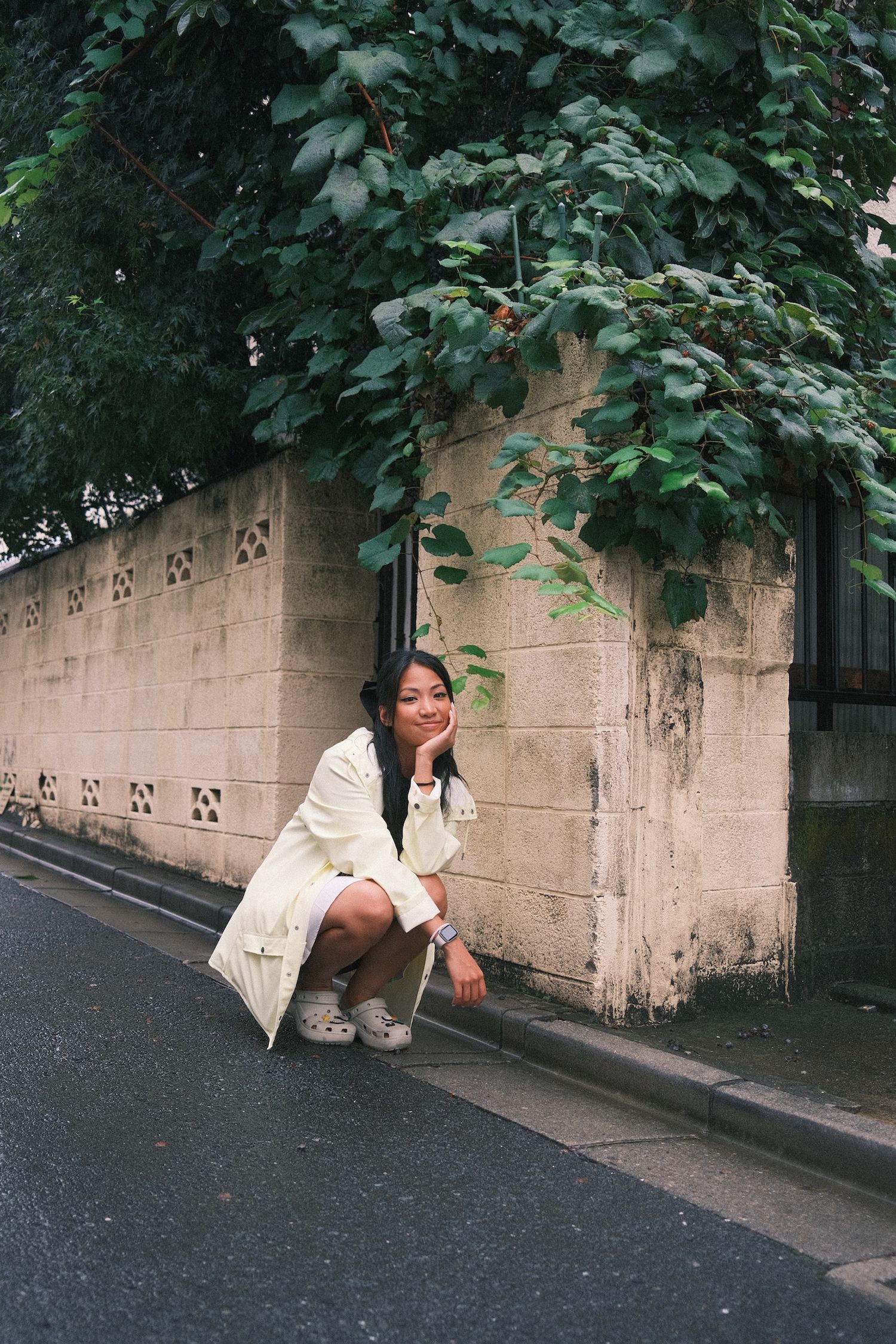 Casual street style photo against stone wall with overhanging green foliage.