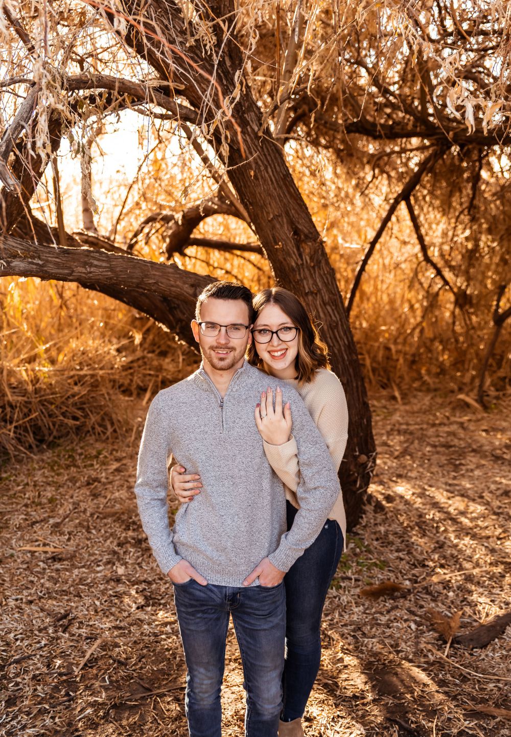 Couple posing for engagement photos in an autumn setting with warm lighting.