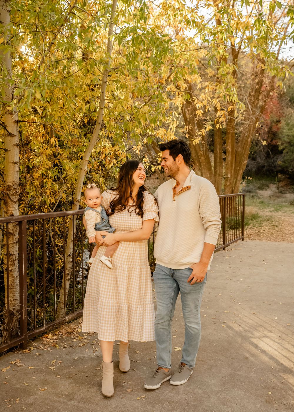 Family walking together on path surrounded by autumn trees and fallen leaves.