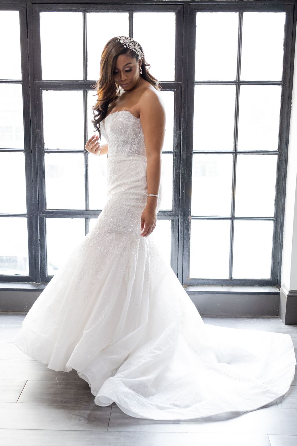 Romantic side view of strapless wedding dress with flowing train by large windows.