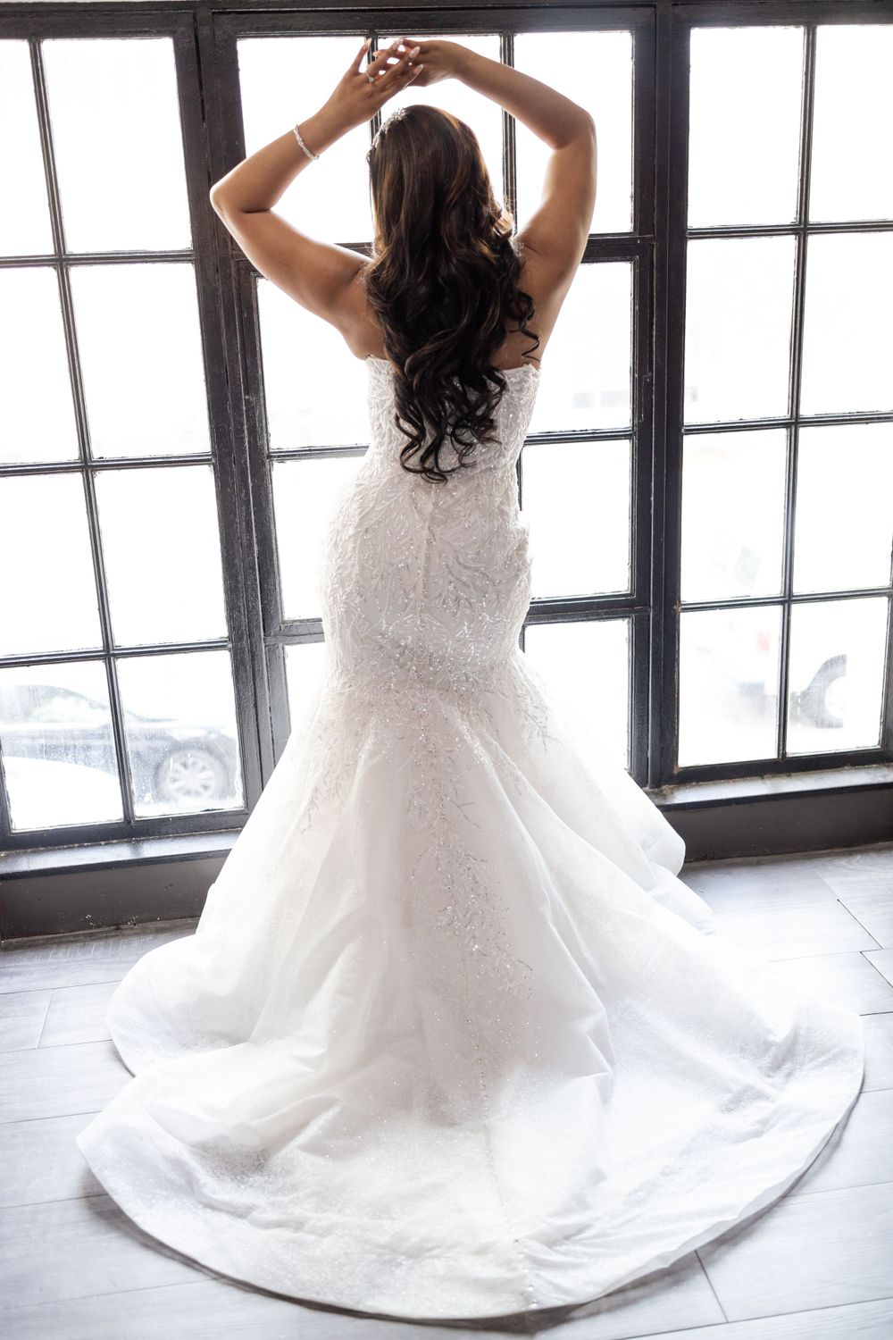 Back view of lace wedding dress with dramatic train against window backdrop.