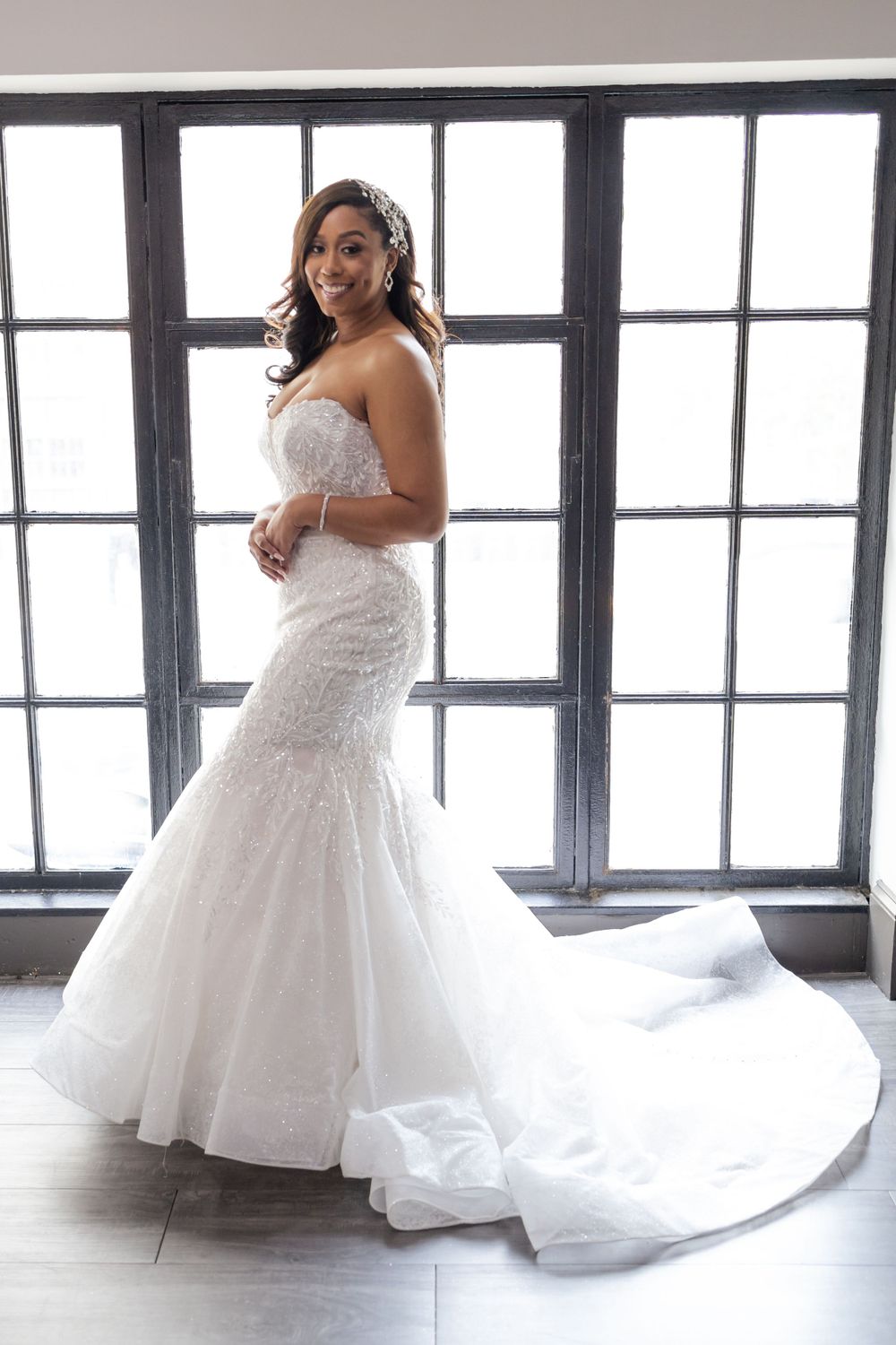 Beautiful mermaid wedding gown with long train photographed by large windows.