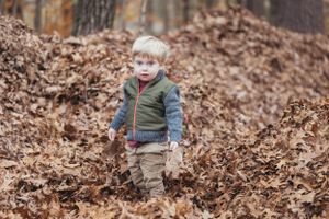 Young child in puffy vest exploring fallen autumn leaves in woods.