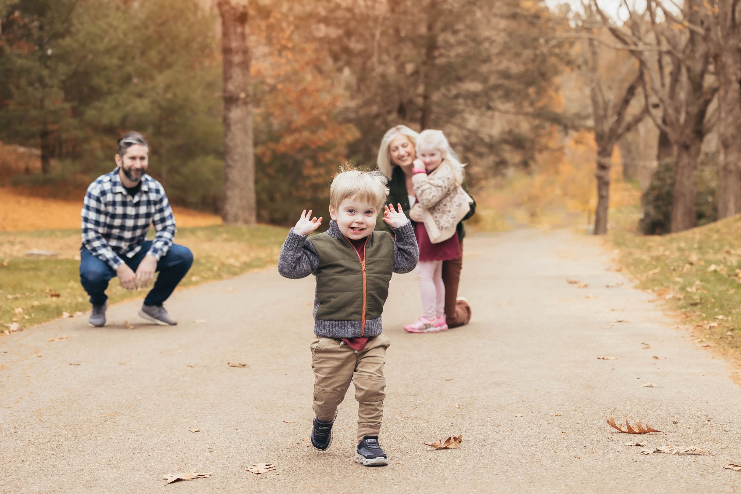 Family having fun running on path through autumn park with fallen leaves.