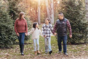 Family taking a stroll together through an evergreen tree farm at sunset.