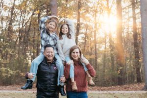Family enjoying outdoor autumn photoshoot with golden sunlight streaming through trees.