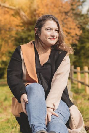 A person in a color block coat sits outdoors against an autumn background.