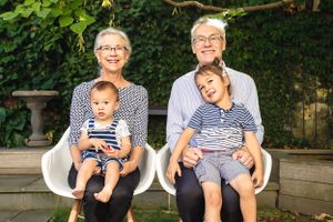 Two adults and two children sitting outdoors on white chairs in garden setting.