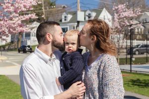 A family shares kisses with their baby under blooming cherry trees.