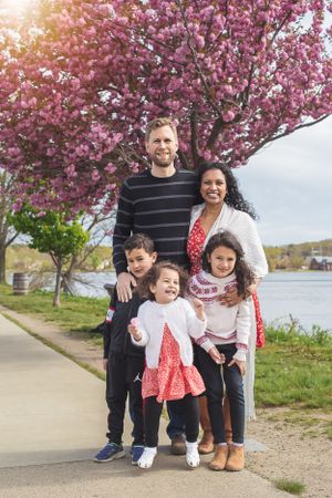 A family poses together under blooming cherry blossoms by a waterfront path.