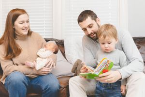 Family relaxing together on couch while reading a storybook to their toddler.
