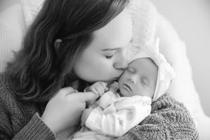 An intimate black and white portrait of a mother bonding with her sleeping newborn.