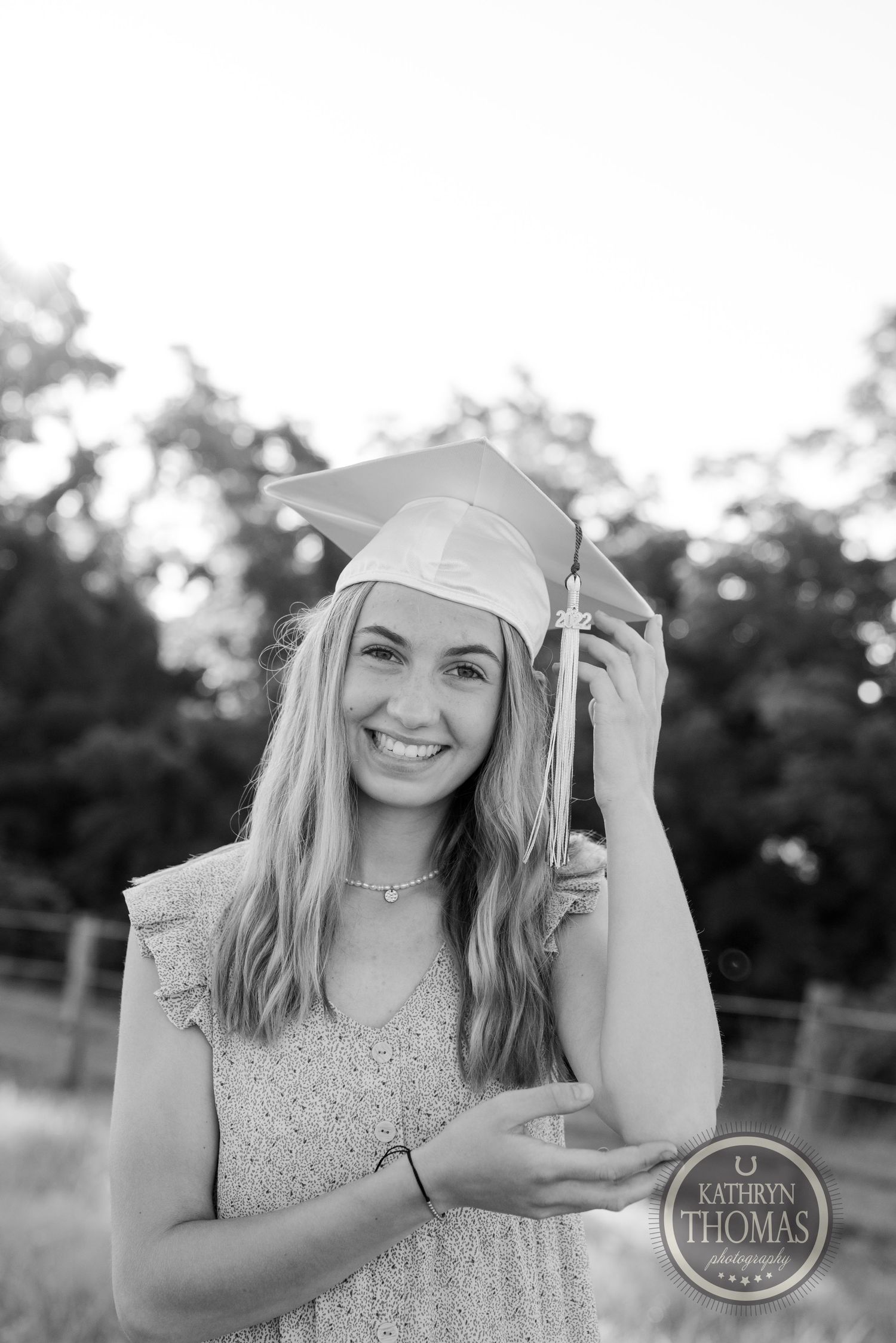 Black and white portrait of a graduate in cap and dress smiling outdoors.
