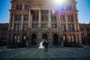 Wedding couple dancing in front of historic courthouse building with sunburst effect.