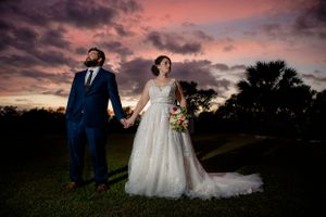 Dramatic sunset wedding portrait with couple holding hands against colorful sky.