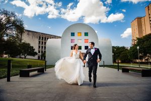 Wedding couple walking together in front of a modern white dome structure under blue skies.