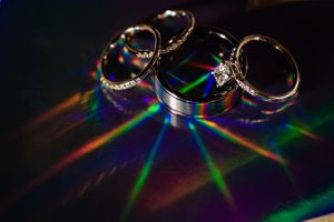 Wedding rings creating rainbow light reflections on dark surface.