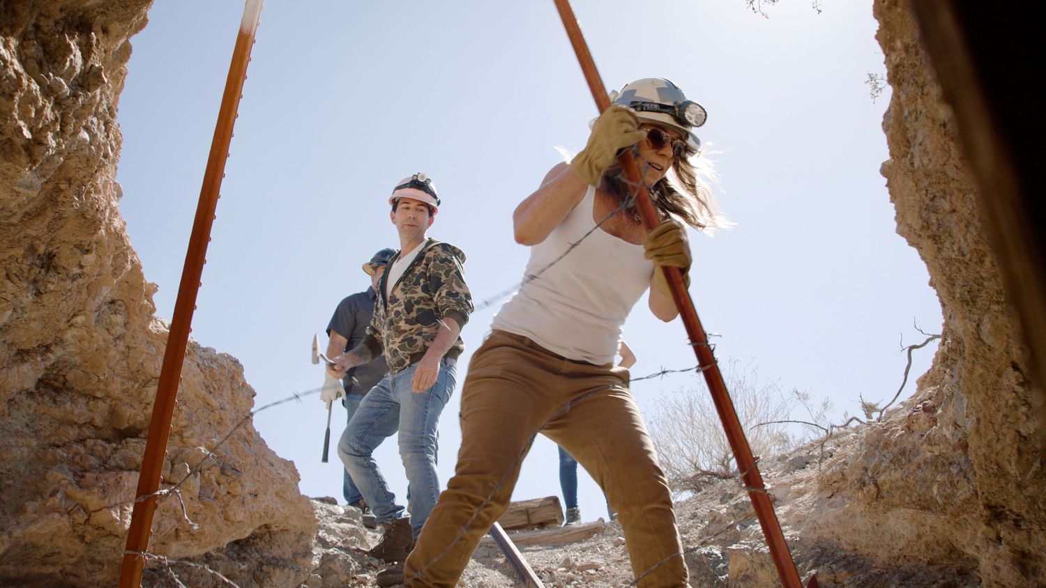 People exploring and climbing through rocky terrain using support poles.