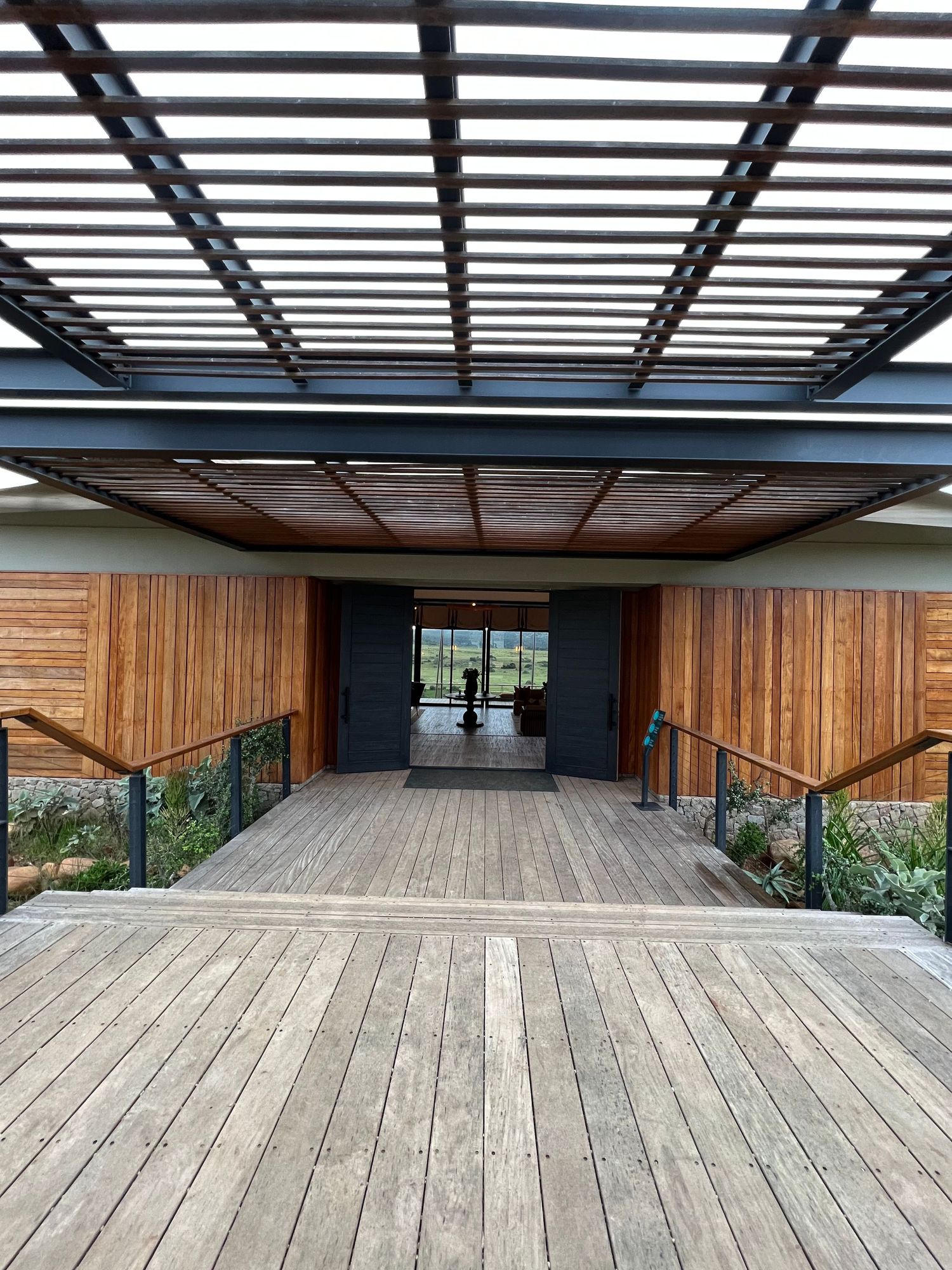 Modern wooden deck with black pergola slats creating geometric shadows on the timber flooring.