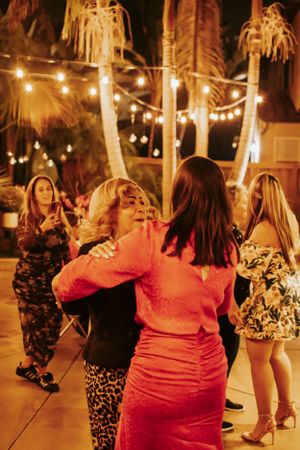 People dancing under strings of lights and palm trees at an outdoor evening celebration.