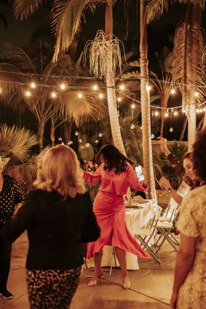 Dancers moving on an outdoor patio beneath illuminated palm trees and string lights.