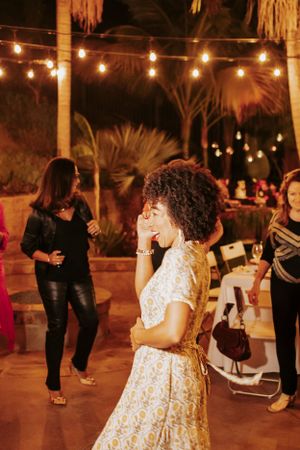 Joyful dance celebration under string lights with tropical palm trees in the evening.