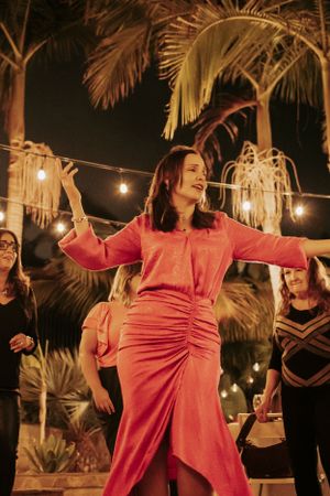 Woman in pink dress dancing under string lights with palm trees in background.