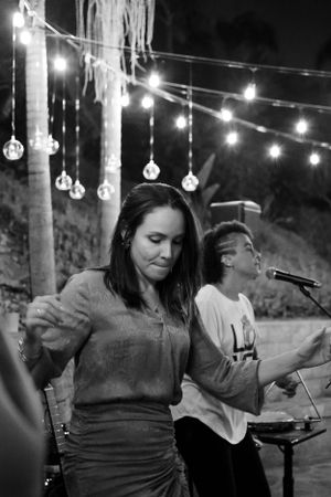 Woman dancing under hanging string lights at night with band performing in background.