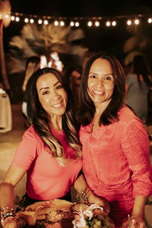 Two friends celebrate at nighttime party wearing coordinating pink outfits under glowing lights.