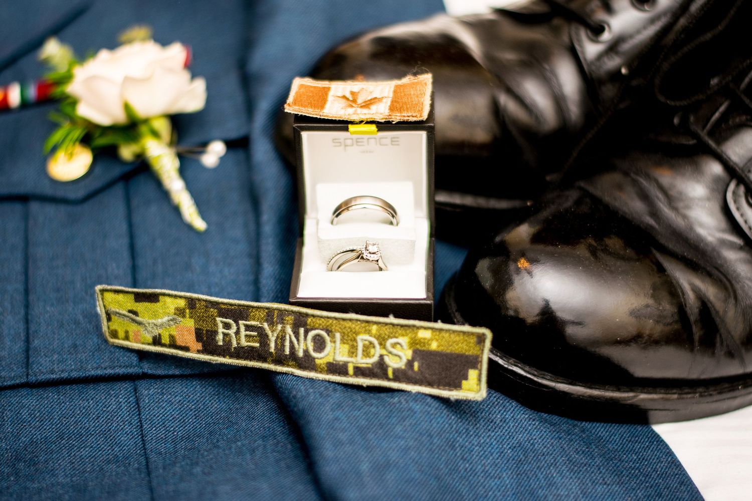 Wedding detail shot showing rings, shoes and a name tag against a navy blue background.
