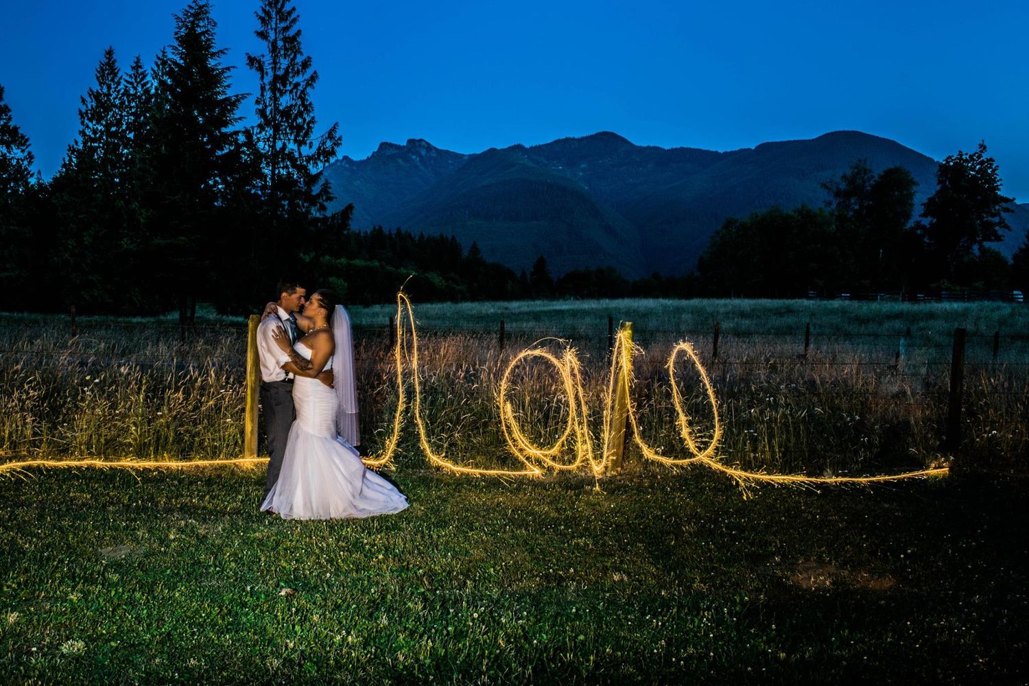 A romantic nighttime photo with 'LOVE' written in light painting against a mountain landscape.