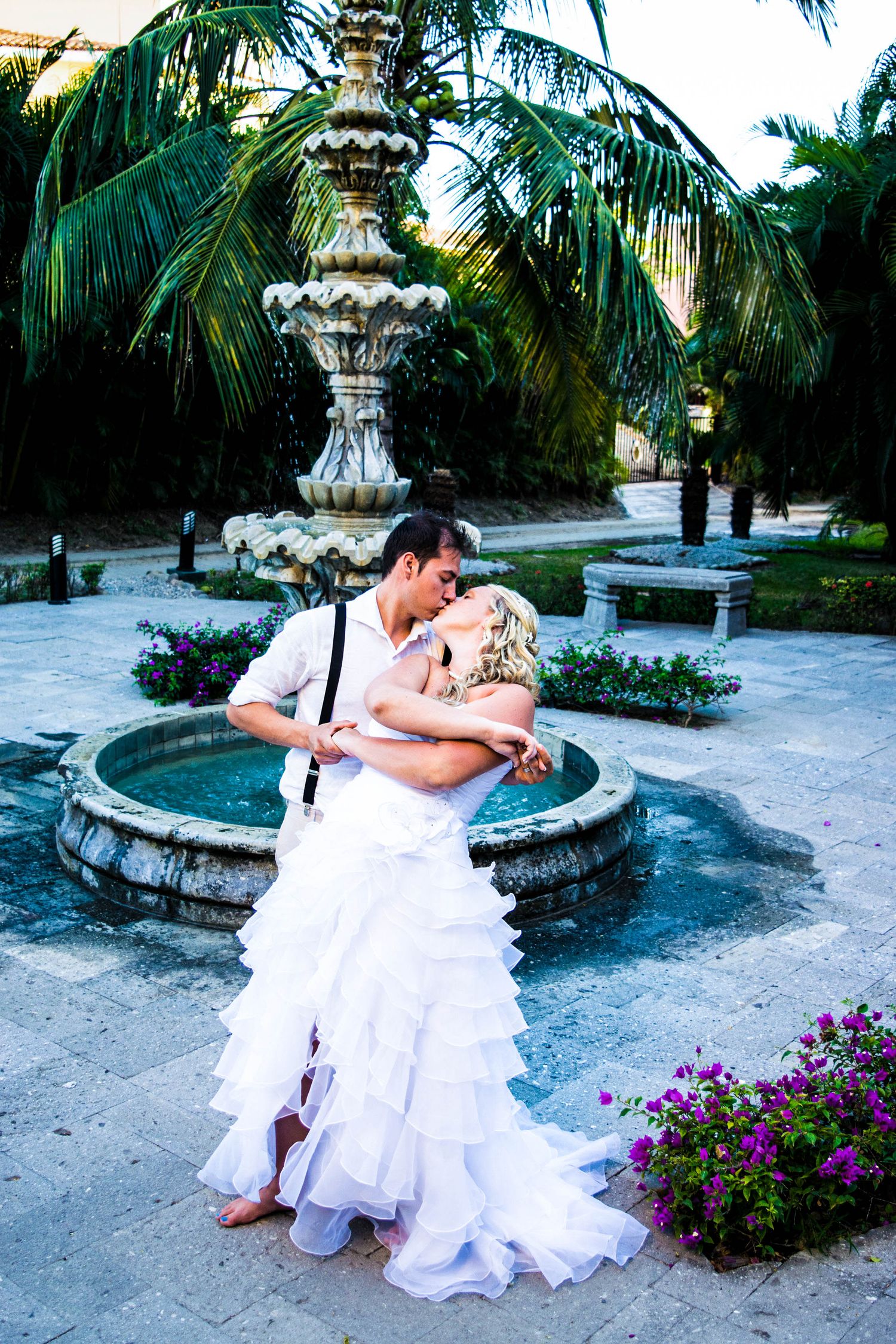 Romantic dance pose by an ornate fountain surrounded by tropical palm trees.
