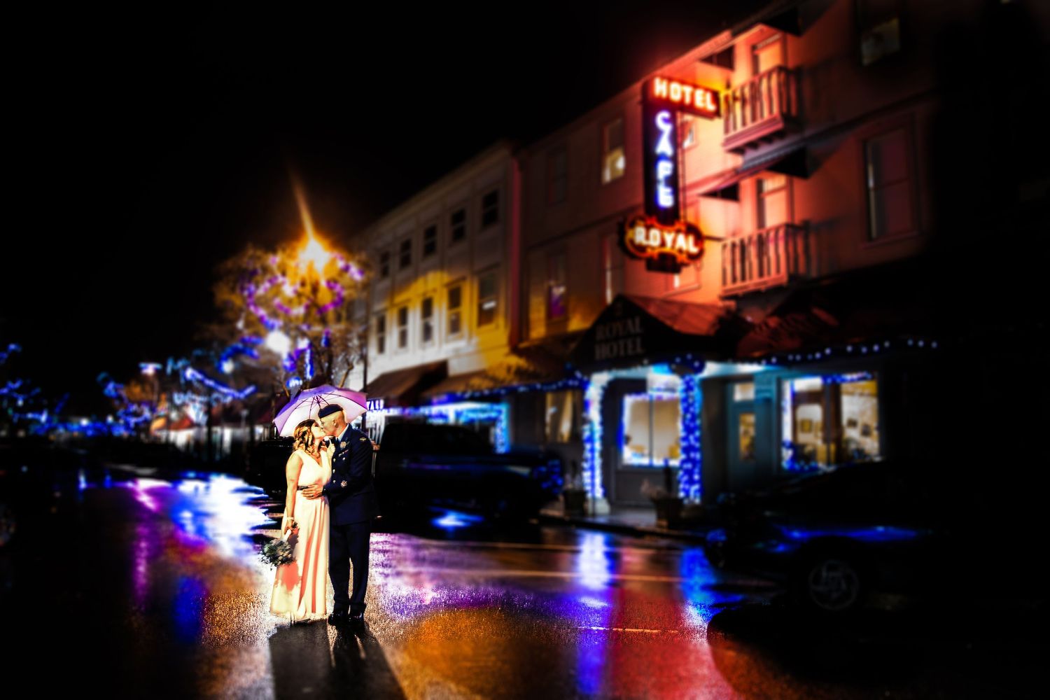 An artistic night wedding photo on a rainy street with colorful neon lights.
