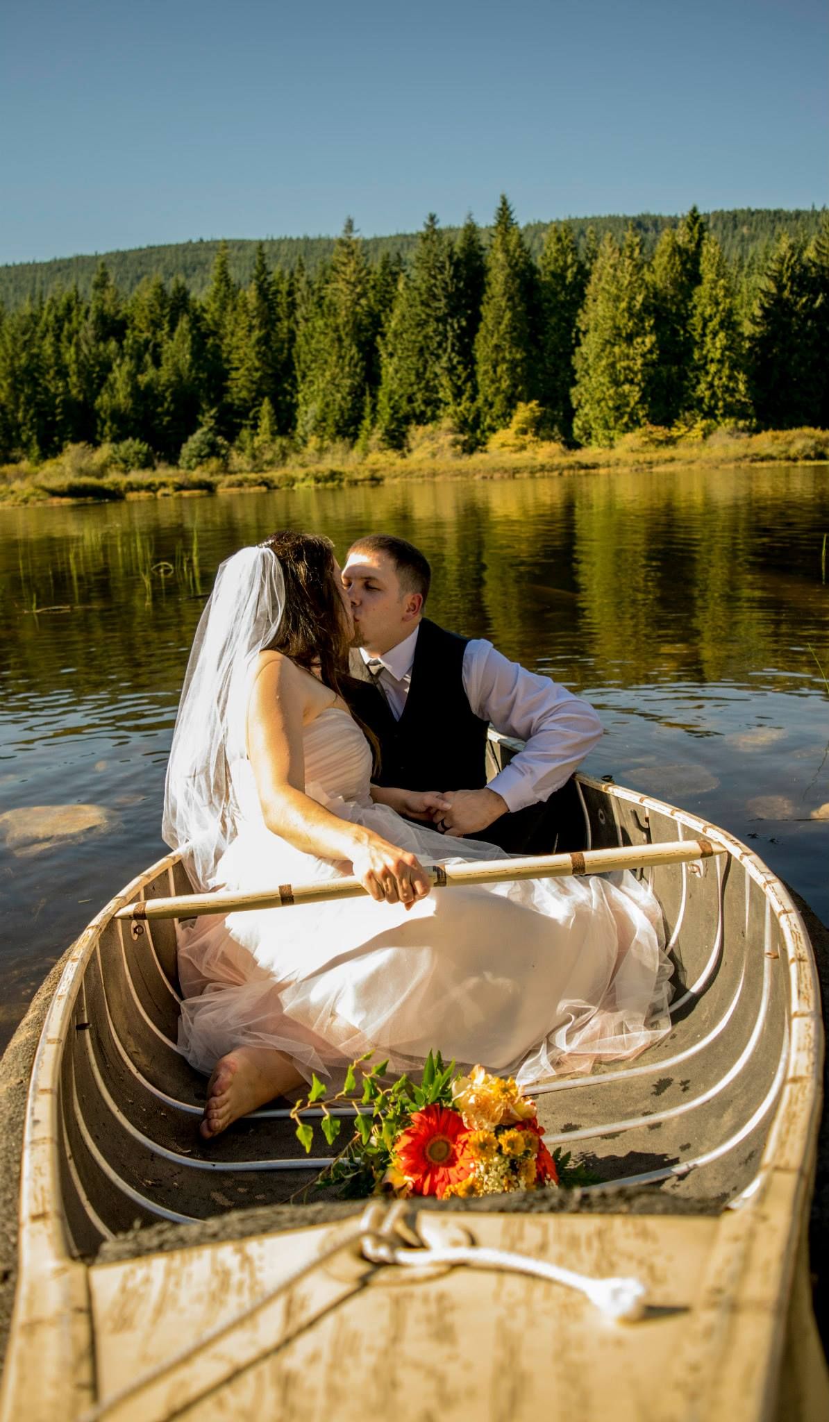 Romantic canoe scene with wedding couple on a serene lake surrounded by evergreen forest.