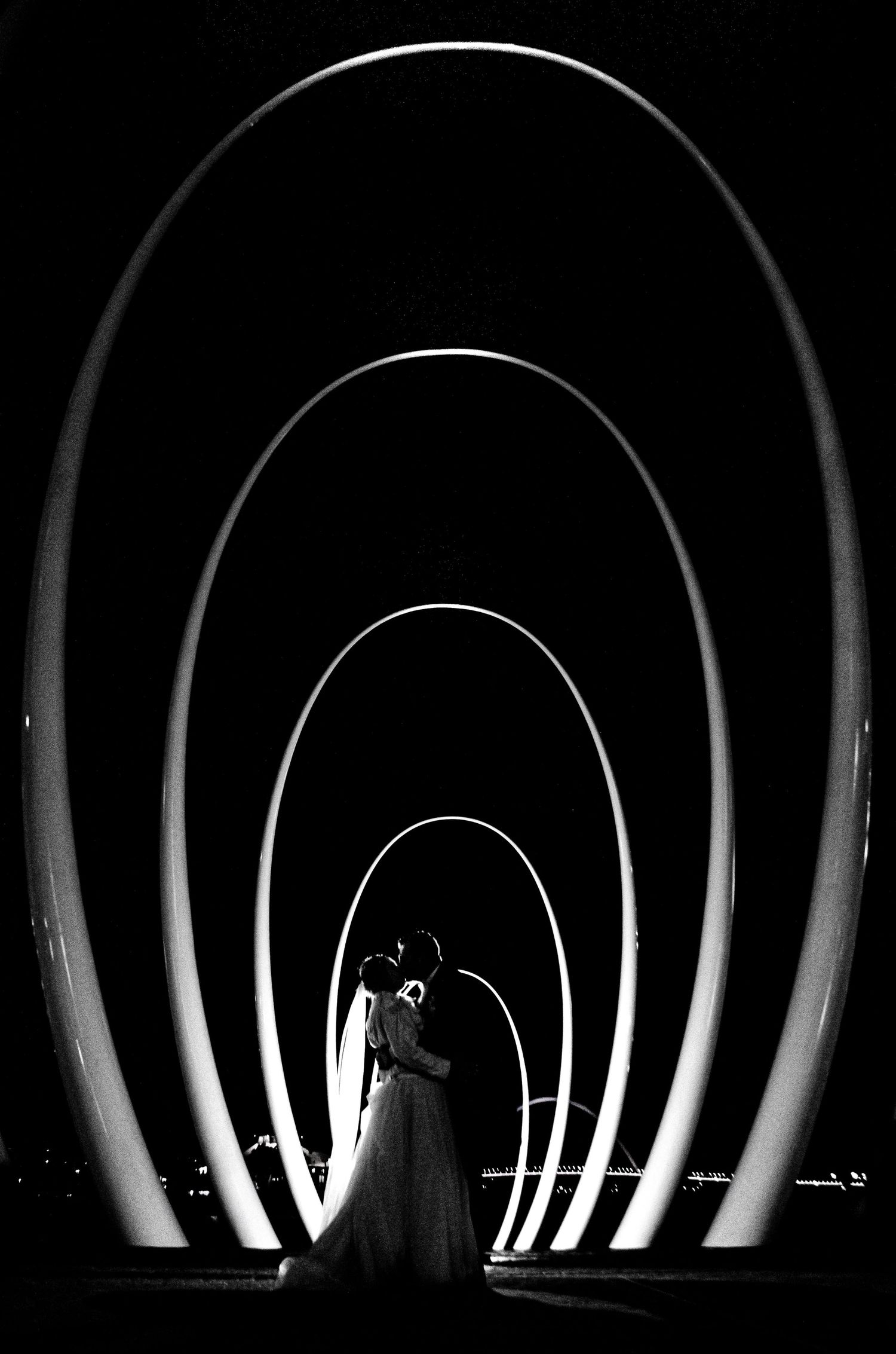 A silhouette of a couple stands in a dramatic archway with concentric illuminated circles.