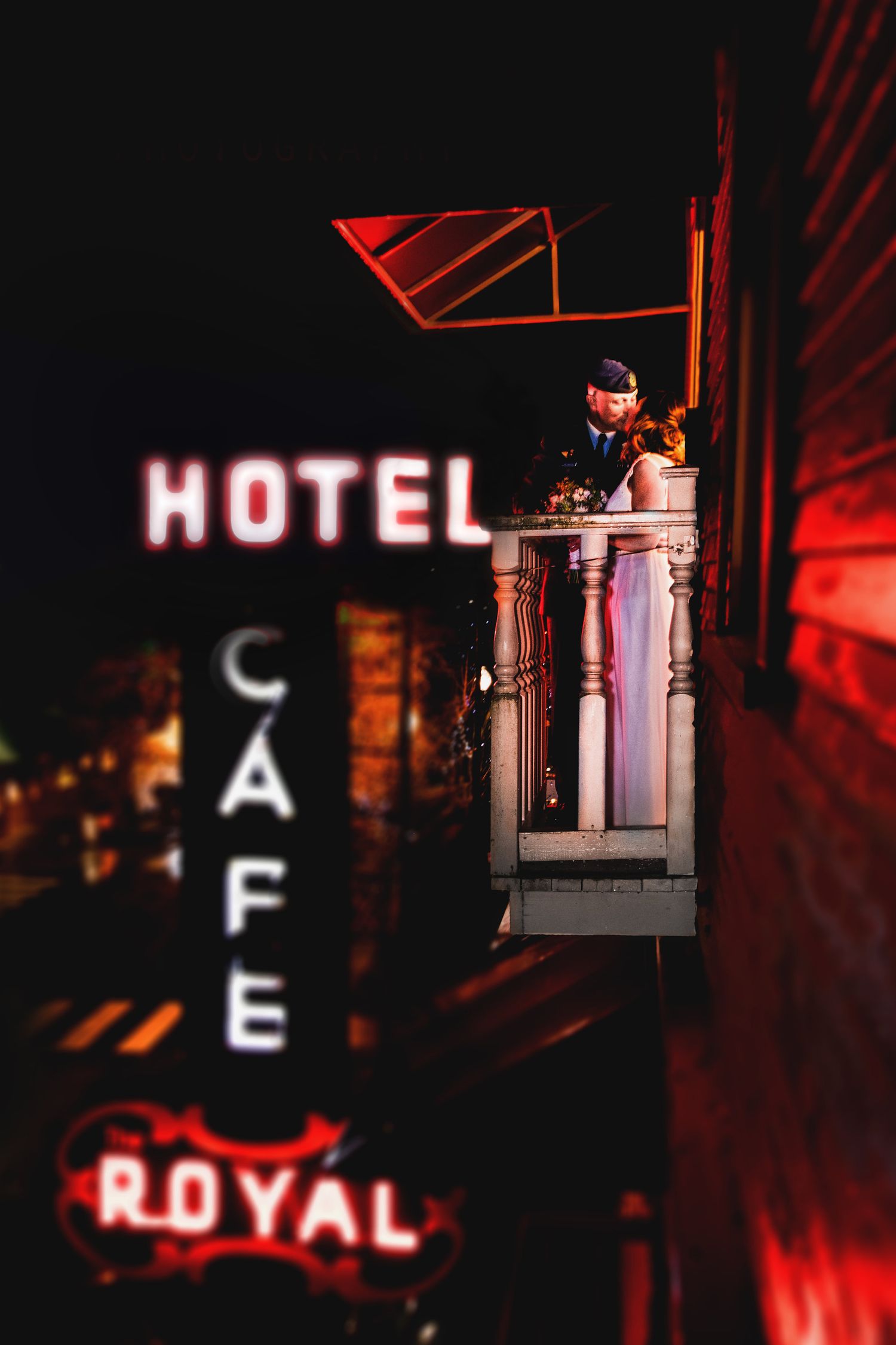 A nighttime wedding portrait on a balcony with vintage hotel neon signs glowing in the background.