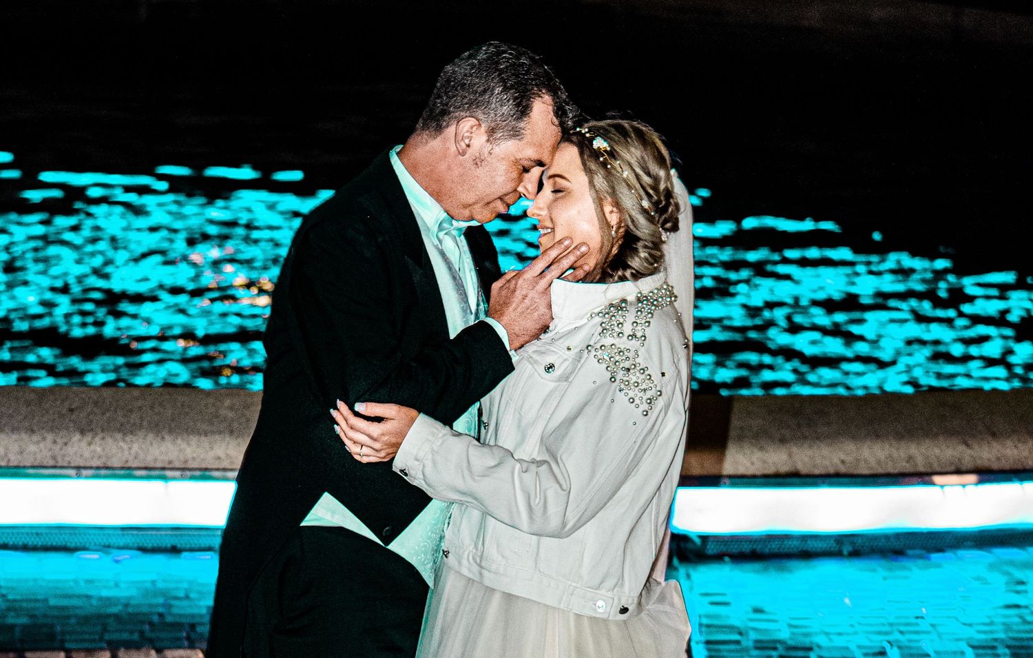 A romantic moment near illuminated turquoise water at night.