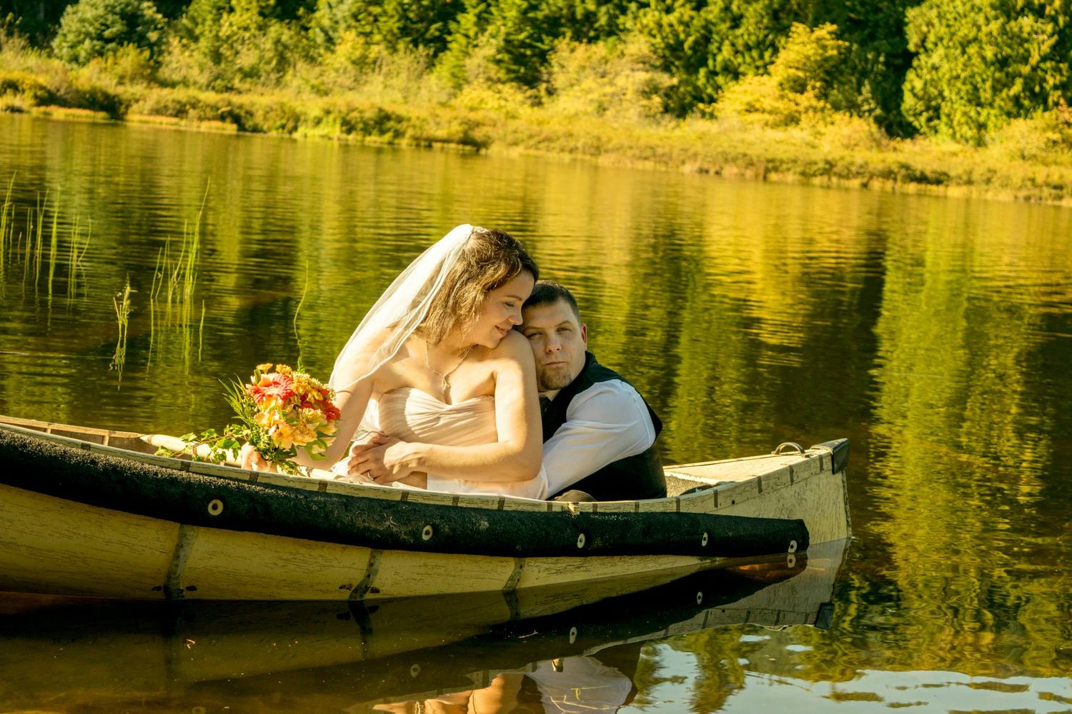 Wedding couple shares intimate moment in wooden canoe on reflective lake during golden hour.